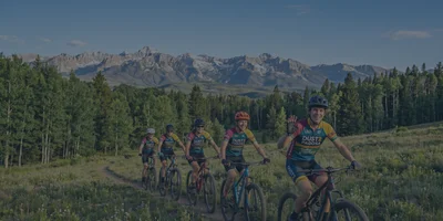 A group of youth mountain bikers from the DUST2 Pagosa team smiling while riding on a scenic trail in the San Juan Mountains of Colorado.